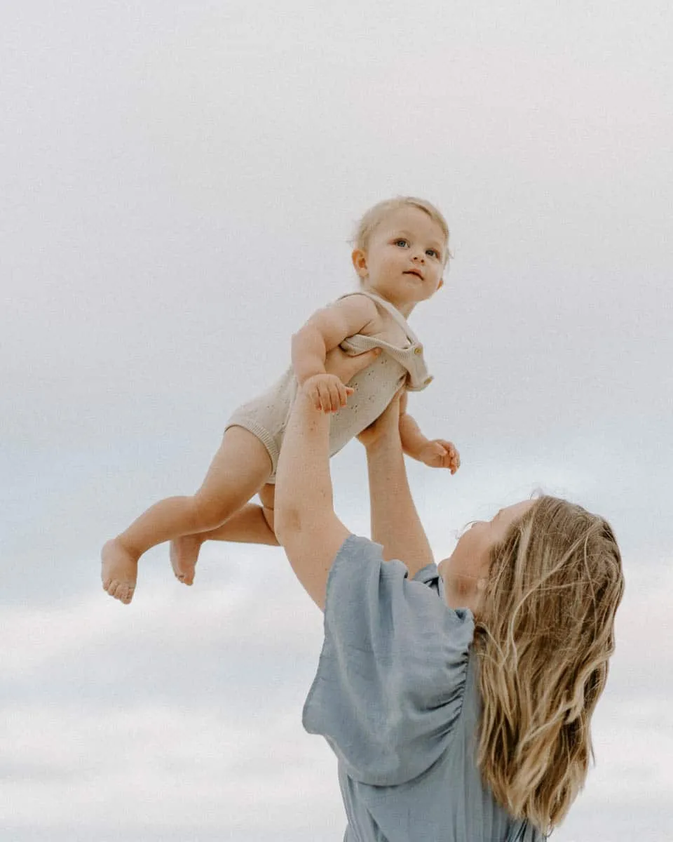 Expecting mother holding her baby during a soft-light beach maternity session