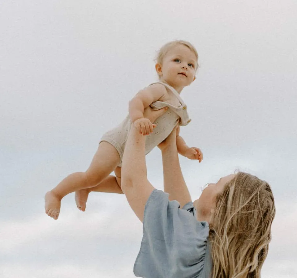 Expecting mother holding her baby during a soft-light beach maternity session