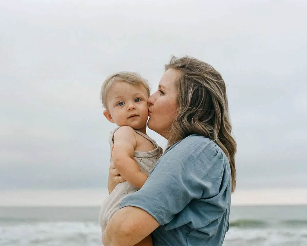 Expecting mother holding her baby during a soft-light beach maternity session