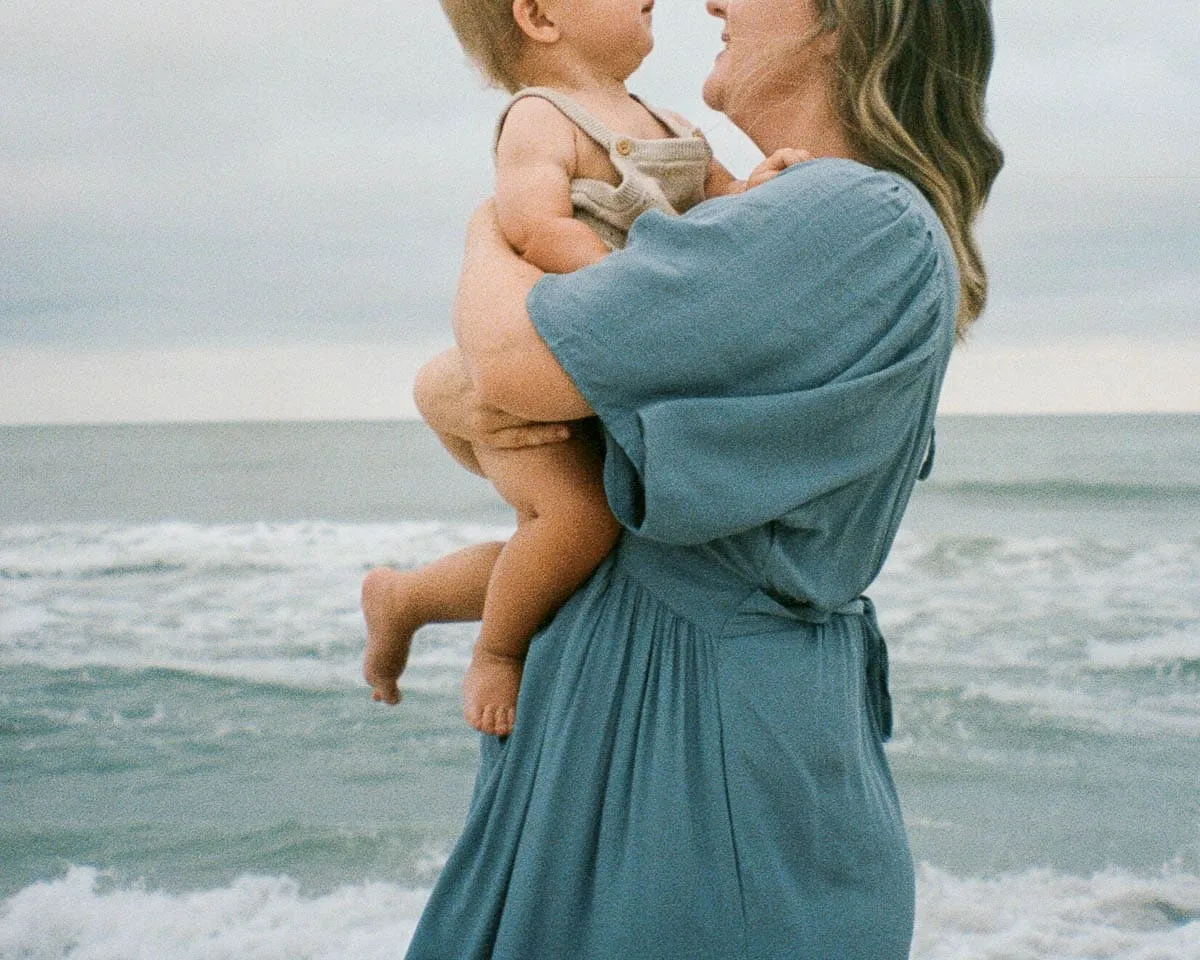 Expecting mother holding her baby during a soft-light beach maternity session