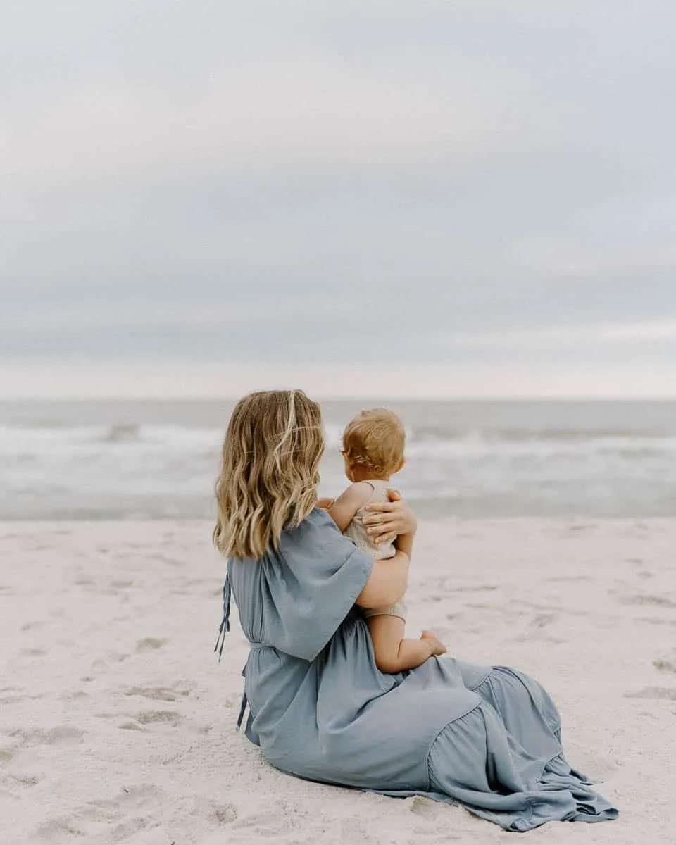 Expecting mother holding her baby during a soft-light beach maternity session