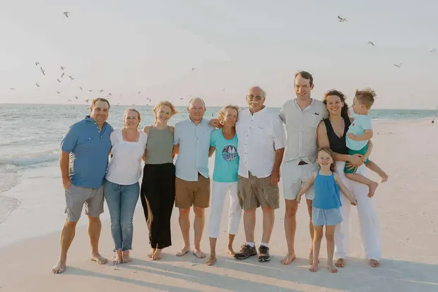 Three generations of a family standing together on the beach at sunset