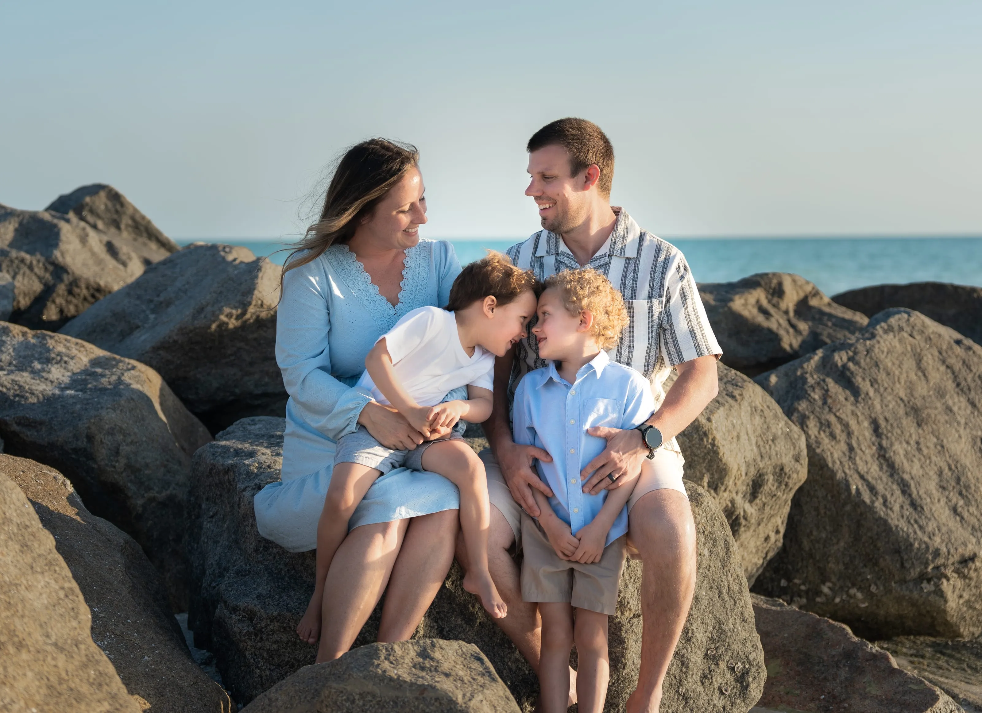 Parents with their two young sons sitting together on beach rocks by the Gulf