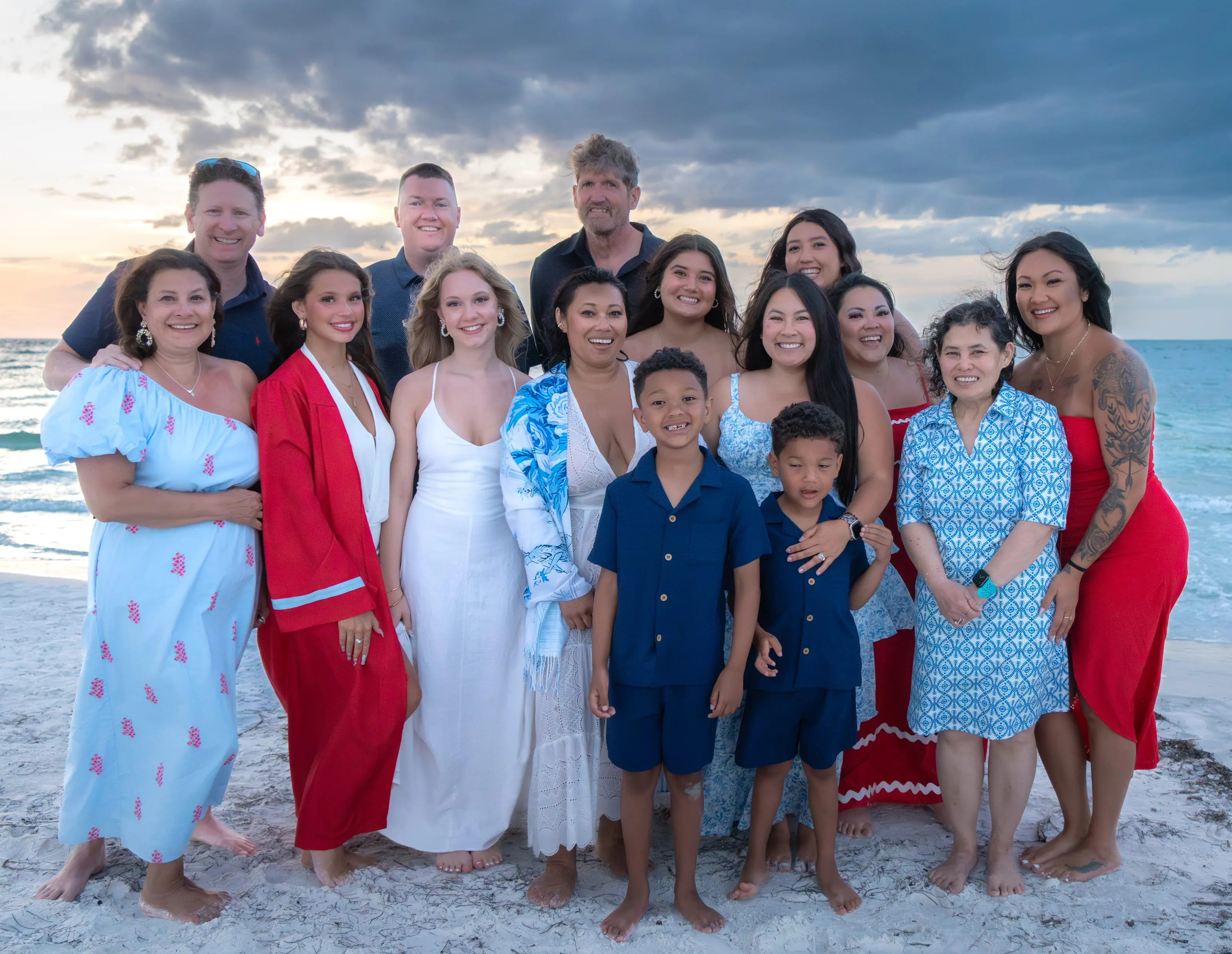 Three generations of an extended family gathered on the sand at dusk