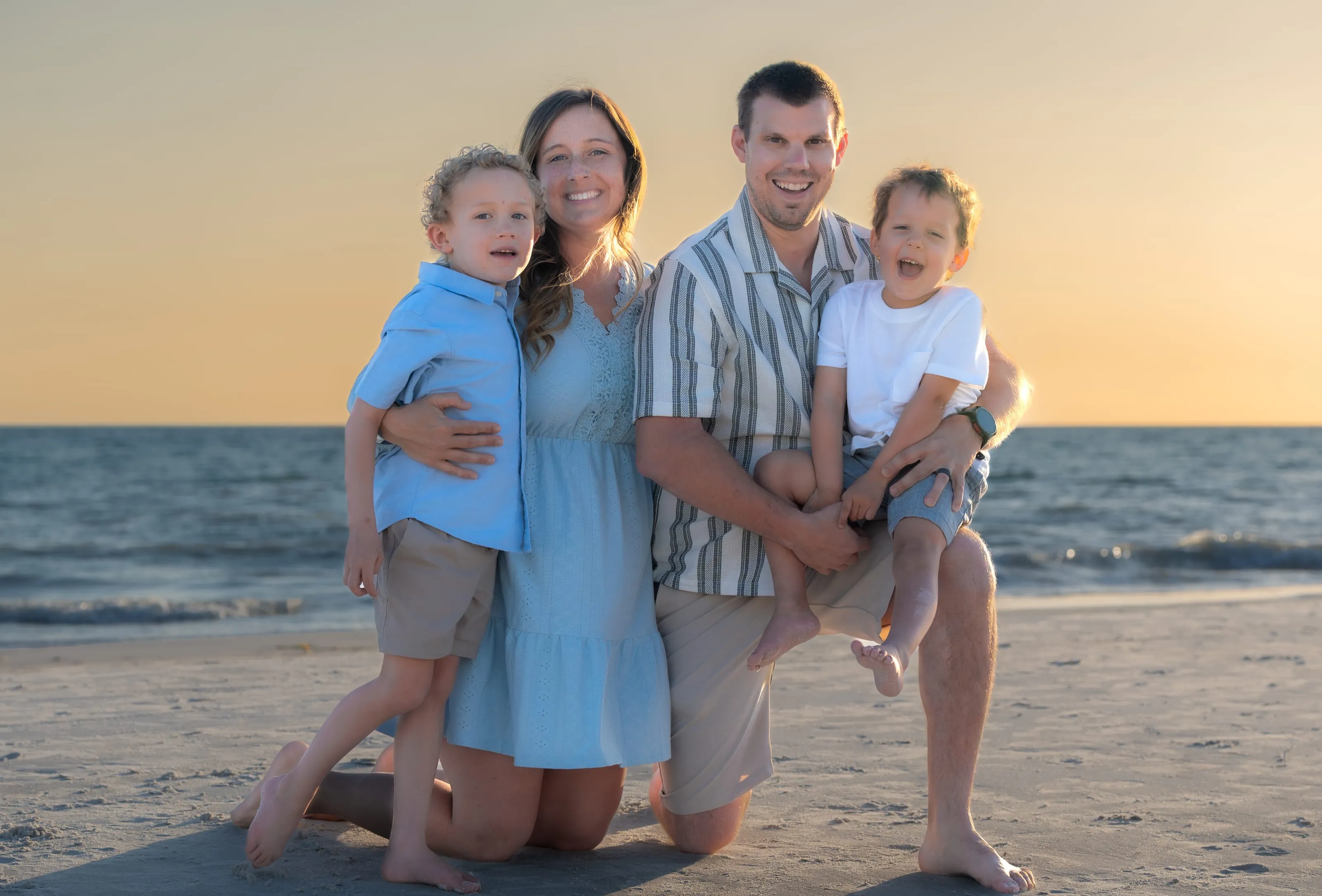 Parents kneeling on the sand with their two boys at sunset