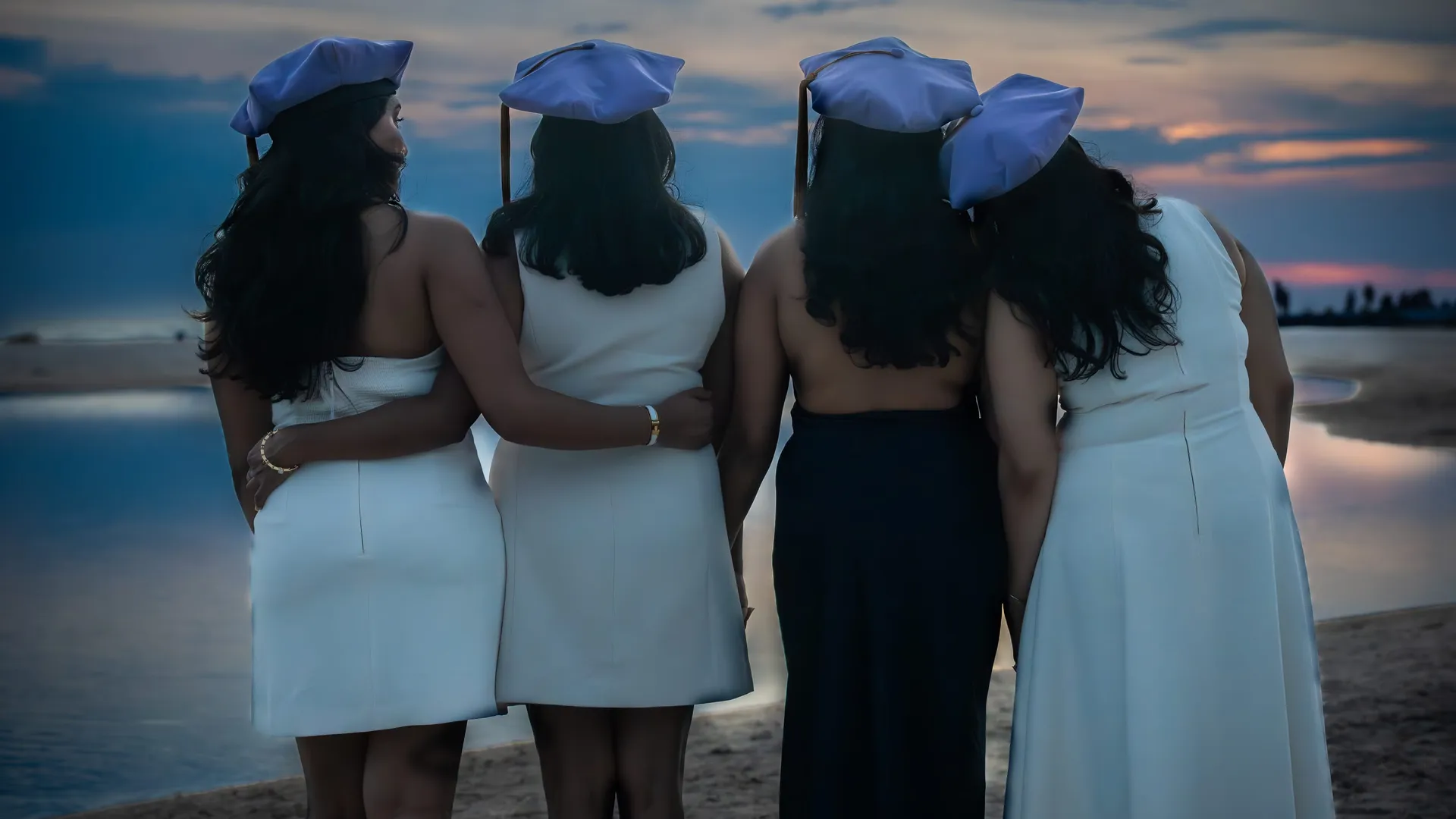 Four graduates in caps looking out over the Gulf at sunset