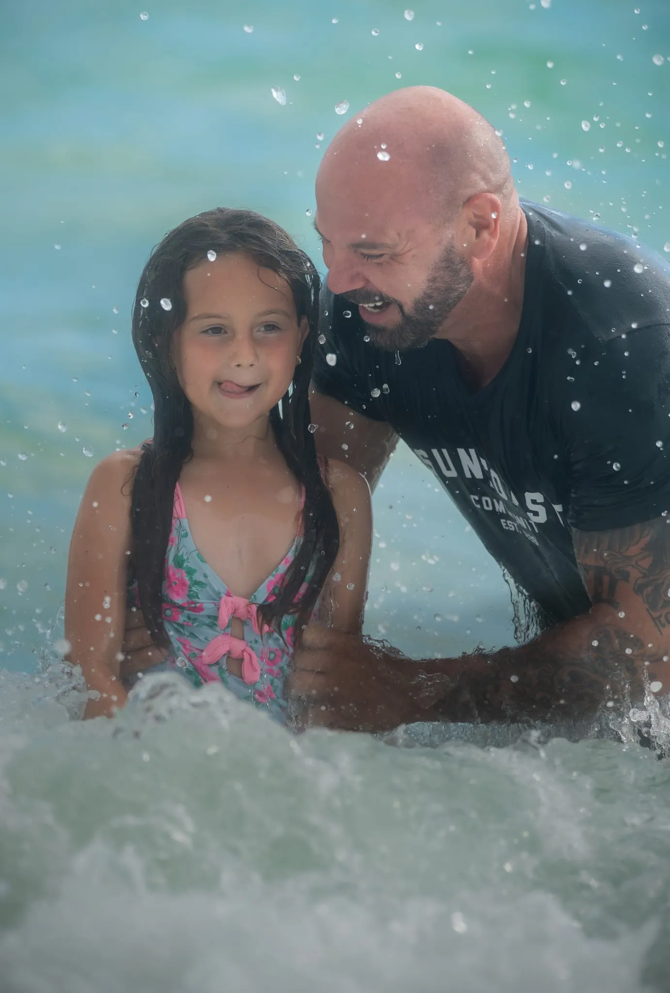 Dad and young daughter laughing in the splash of a Gulf wave
