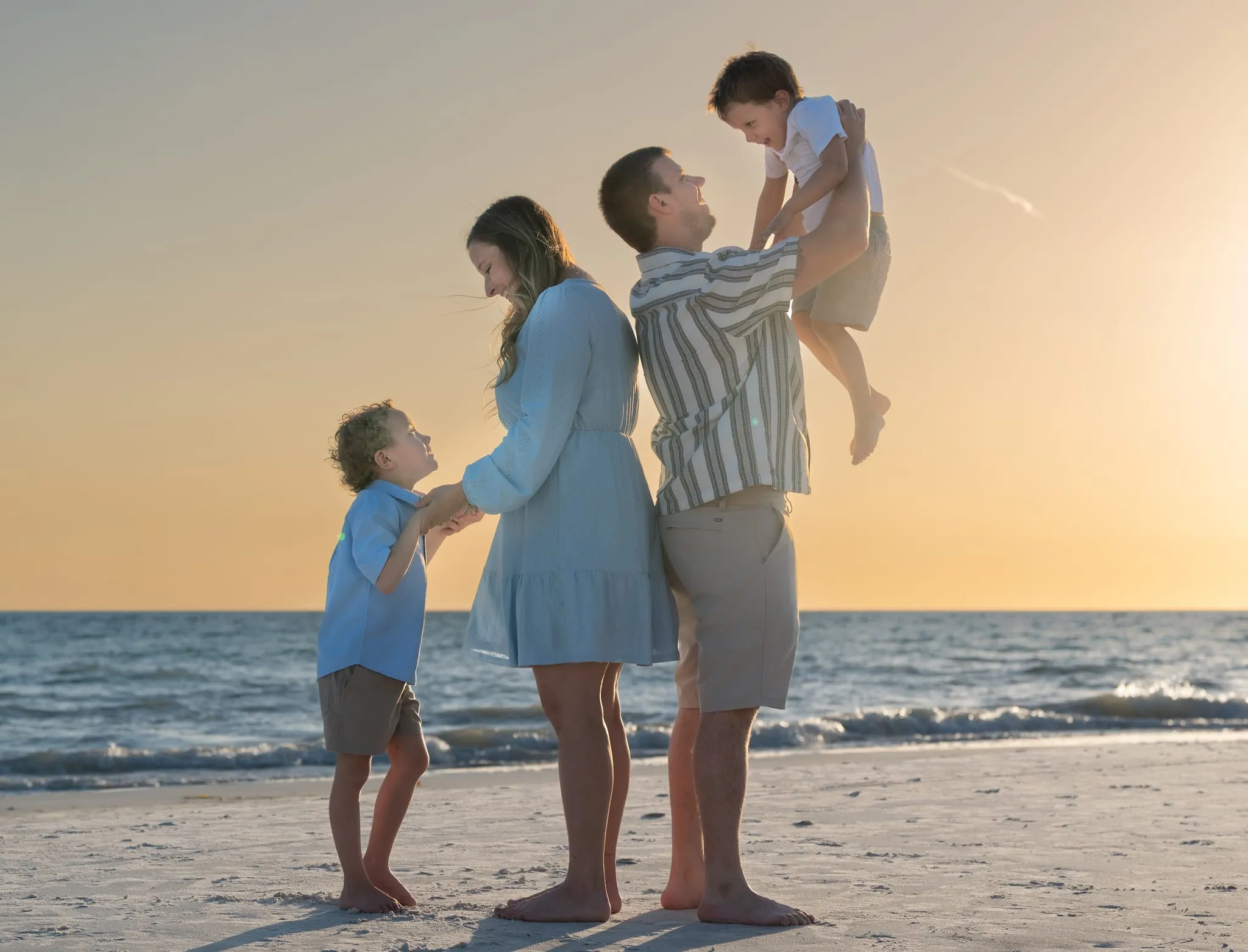 Parents playing with their two boys on the beach at sunset